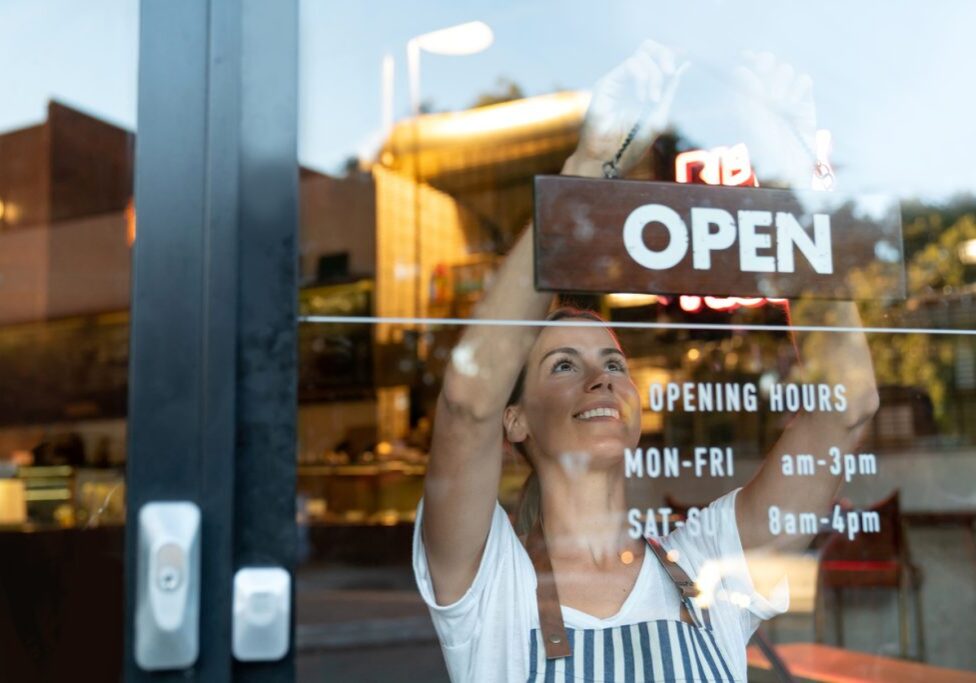 Happy business owner hanging an open sign at a cafe