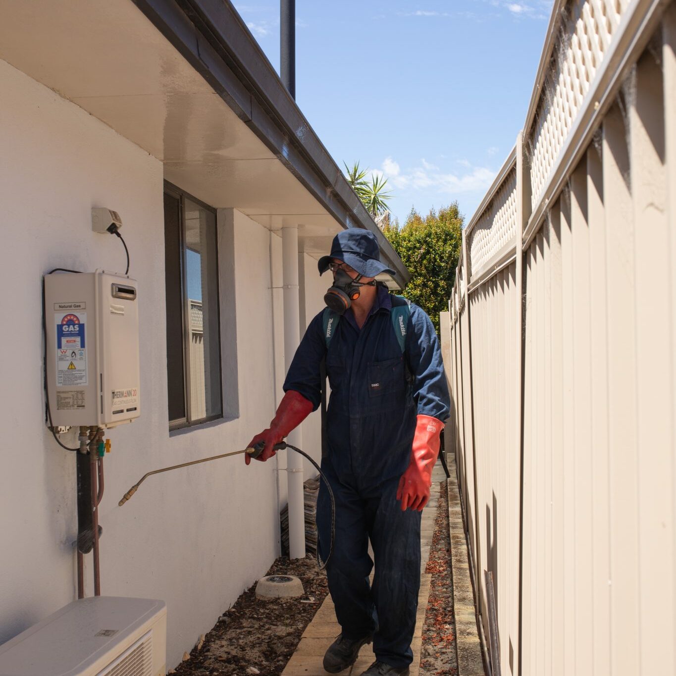 Technician spraying pesticide outside house wall.