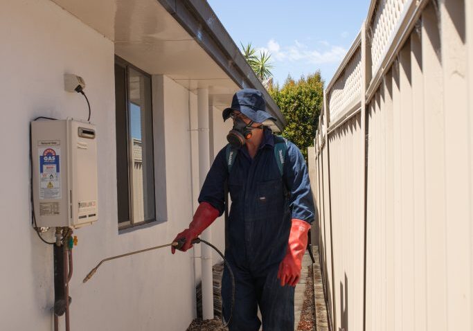 Technician spraying pesticide outside house wall.